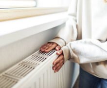 Personne réchauffant ses mains près d’un appareil de chauffage résidentiel, illustrant le confort d’un système de chauffage moderne au Québec.