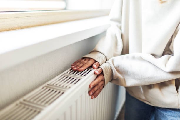 Personne réchauffant ses mains près d’un appareil de chauffage résidentiel, illustrant le confort d’un système de chauffage moderne au Québec.