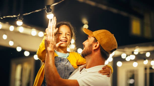 Père aidant sa fille à décorer des lumières extérieures lors d’une soirée.